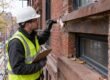 Contractor inspecting brick mortar joints and window lintel on an NYC brownstone facade before winter